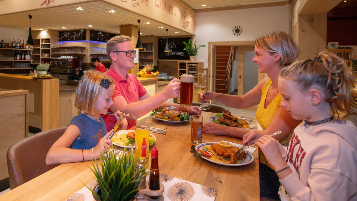 Familie prostet sich zu beim Halbpensions-Abendessen im Restaurant Menüwirt — Schnitzel und Beilagen auf dem Tisch