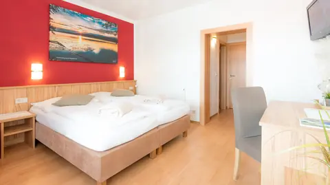 Kernbuche-Doppelzimmer im Gasthof Menüwirt — Doppelbett mit roter Akzentwand und Holzmöbel